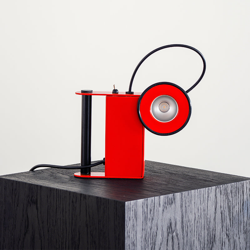 Modern red desk lamp with sleek design, stylishly illuminating a dark wooden surface.